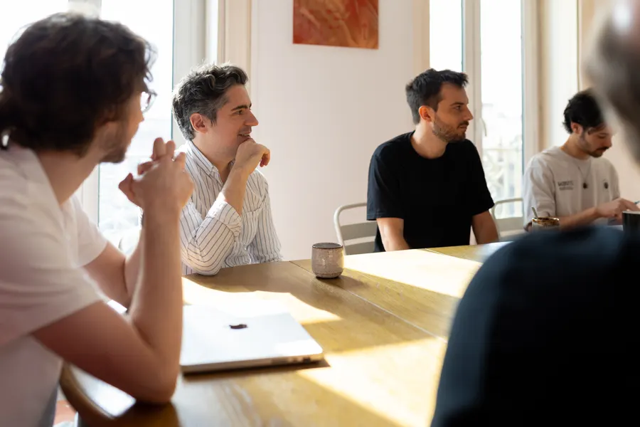 L’équipe en discussion autour d’une grande table en bois, dans une pièce baignée de lumière